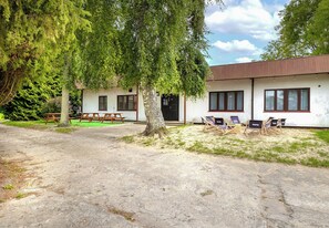 A building with a white facade, multiple windows, and a covered outdoor seating area with chairs. - Ale Fale Trzęsacz Apartment #1 (Trzęsacz)