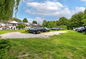 A parking area with several cars, a building with solar panels, and a grassy field. - Ale Fale Trzęsacz Apartment #1 (Trzęsacz)