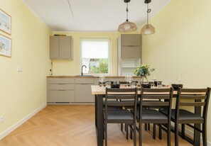 A modern kitchen with wooden cabinets, a dining table set for four, and a window with a view of greenery. - Ale Fale Trzęsacz Apartment #1 (Trzęsacz)