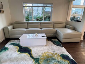 Ein Wohnzimmer mit einem beigefarbenen Ecksofa, einem weißen Couchtisch und einem großen abstrakten Teppich.