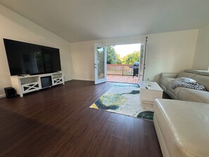Ein Wohnzimmer mit Flachbildfernseher, einer Couch, einem Couchtisch und einer Tür zu einer Terrrasse.