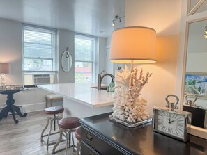 A modern kitchen with a central island, bar stools, a large lamp, and a decorative coral piece. - State + Main Condo | Downtown Luxury Studio (Harbor Springs)