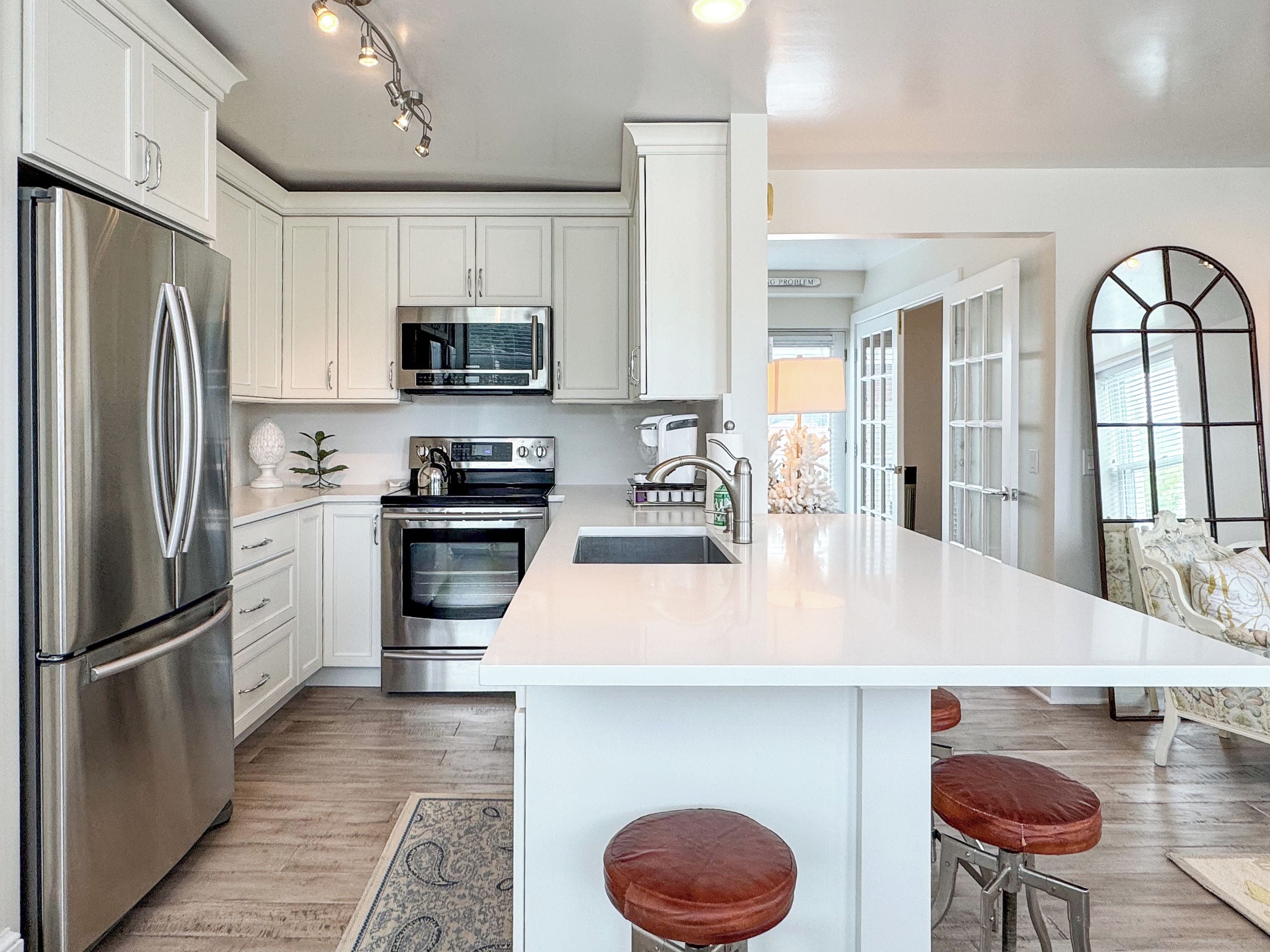 A modern kitchen with stainless steel appliances, a central island with stools, and a view to the living area.