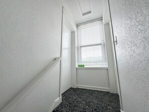 A narrow hallway with a window, white textured walls, and a patterned carpet. - State + Main Condo | Downtown Luxury Studio (Harbor Springs)