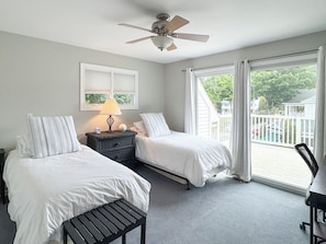 A bedroom with two beds, a nightstand with a lamp, a ceiling fan, and a view of the outside. - Colonial Weque Condo | Views of the Harbor (Harbor Springs)