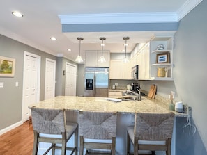 A kitchen with a central island, pendant lights, and a refrigerator. - Colonial Weque Condo | Views of the Harbor (Harbor Springs)
