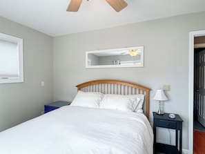 A bedroom with a bed, a nightstand, a lamp, a mirror, and a ceiling fan. - Colonial Weque Condo | Views of the Harbor (Harbor Springs)