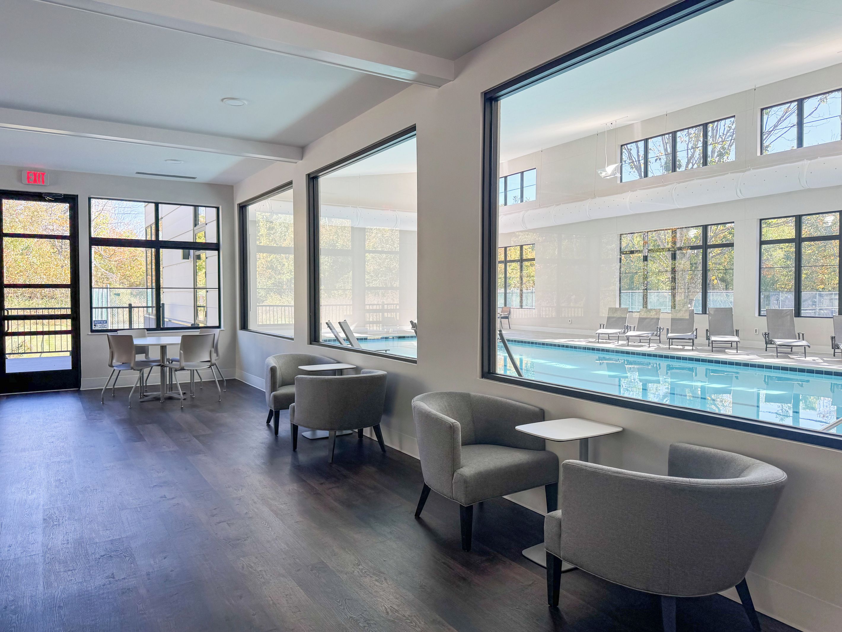 A hotel room with large windows, a pool view, and a seating area with chairs and tables.
