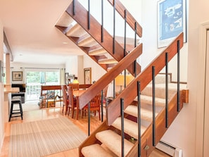 Eine hölzerne Treppe mit Teppichstufen führt zu einem Essbereich mit Tisch und Stühlen.