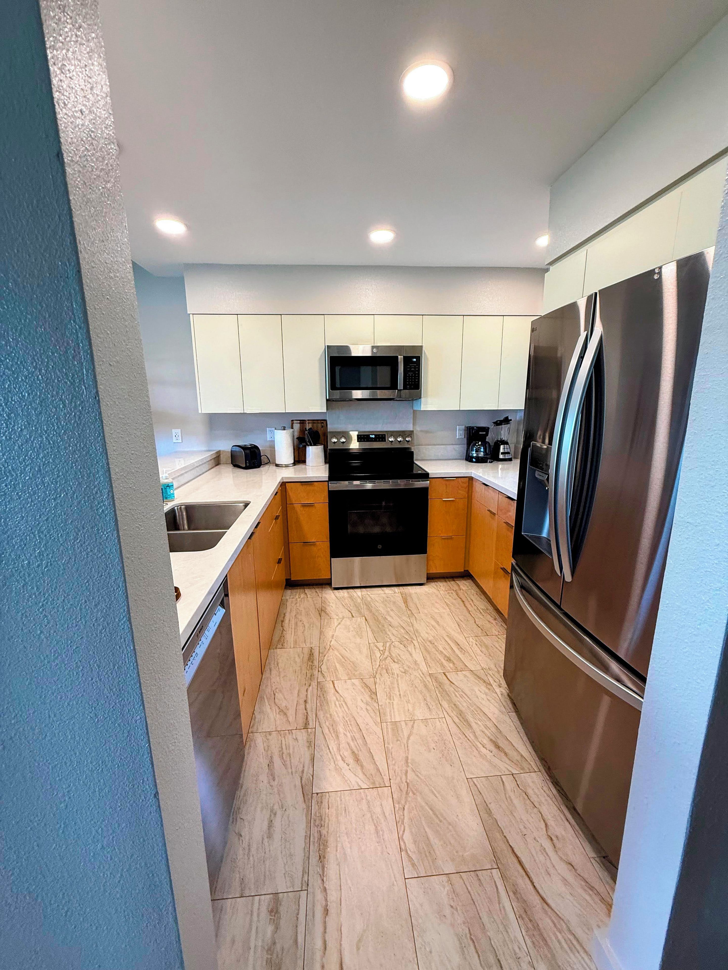 A modern kitchen with stainless steel appliances, wooden cabinets, and a marble floor.