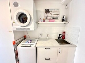 A compact kitchen with a washing machine, a small sink, and a shelf with a welcome sign. - Murlong Cres Tallebudgera Creek - 2Bed Waterfront (Gold Coast)