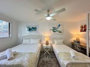A hotel room with two single beds, a ceiling fan, artwork on the walls, and a window with blinds. - Murlong Cres Tallebudgera Creek - 2Bed Waterfront (Gold Coast)