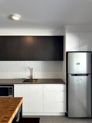 A modern kitchen with white cabinetry, a stainless steel refrigerator, and a wooden table. - Murlong Cres Tallebudgera Creek - 2Bed Waterfront (Gold Coast)