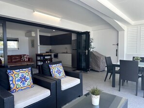 Un espace de vie moderne comprenant un ensemble de canapés, une table à manger et un coin cuisine visible à travers une porte ouverte.