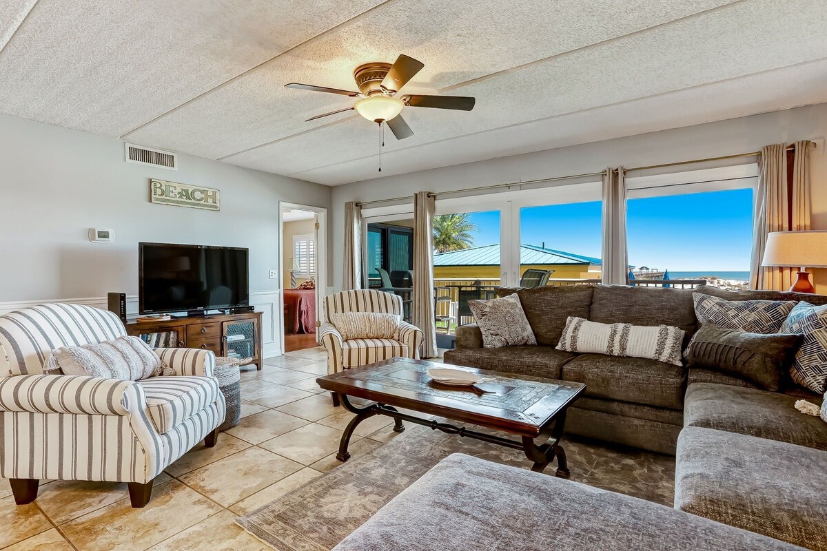 A spacious living room with a television, striped armchairs, a sofa, and a ceiling fan.