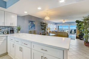 A modern kitchen with white cabinets, a large island, and a dining area with a yellow sofa. - 303 Atlantis 2 Bedroom Condo (Fernandina Beach)
