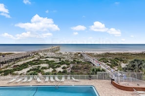 A beachside view with a wooden pier, a swimming pool, and lounge chairs. - 303 Atlantis 2 Bedroom Condo (Fernandina Beach)