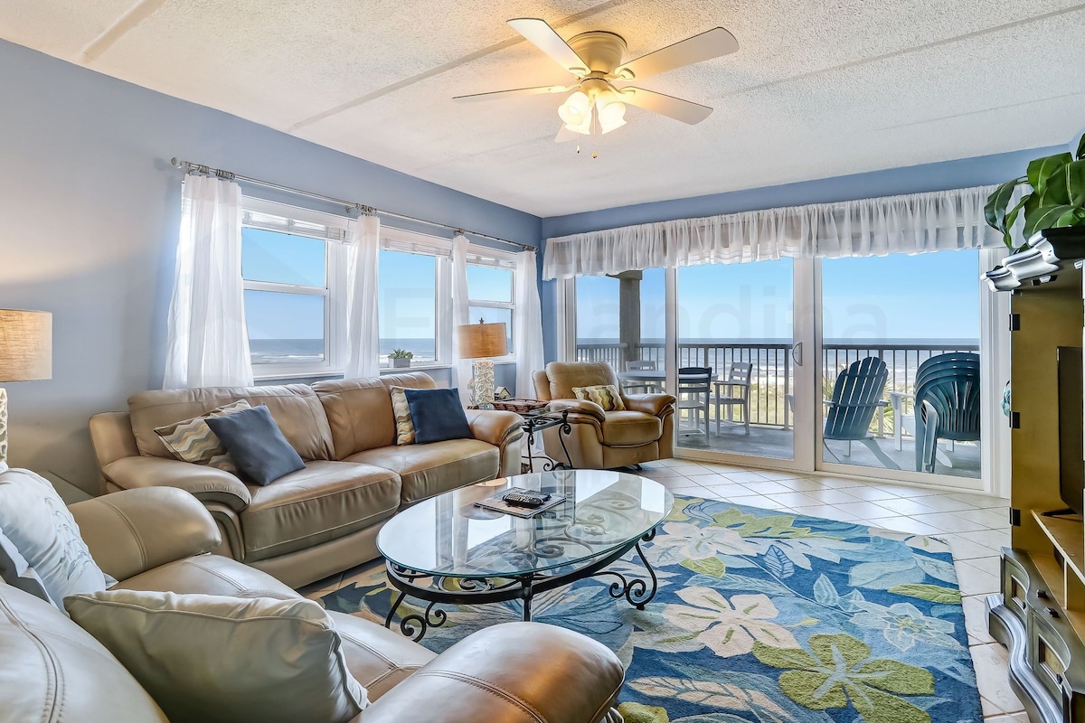 A living room with a glass coffee table, leather sofas, and a view to the outside.