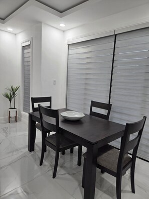 A modern dining area with a dark wooden table and chairs, a white bowl on the table, and a potted plant to the side. - Charisma Airbnb (Kingston)
