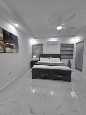 A bedroom with a bed, nightstands, a ceiling fan, and a painting on the wall. - Charisma Airbnb (Kingston)