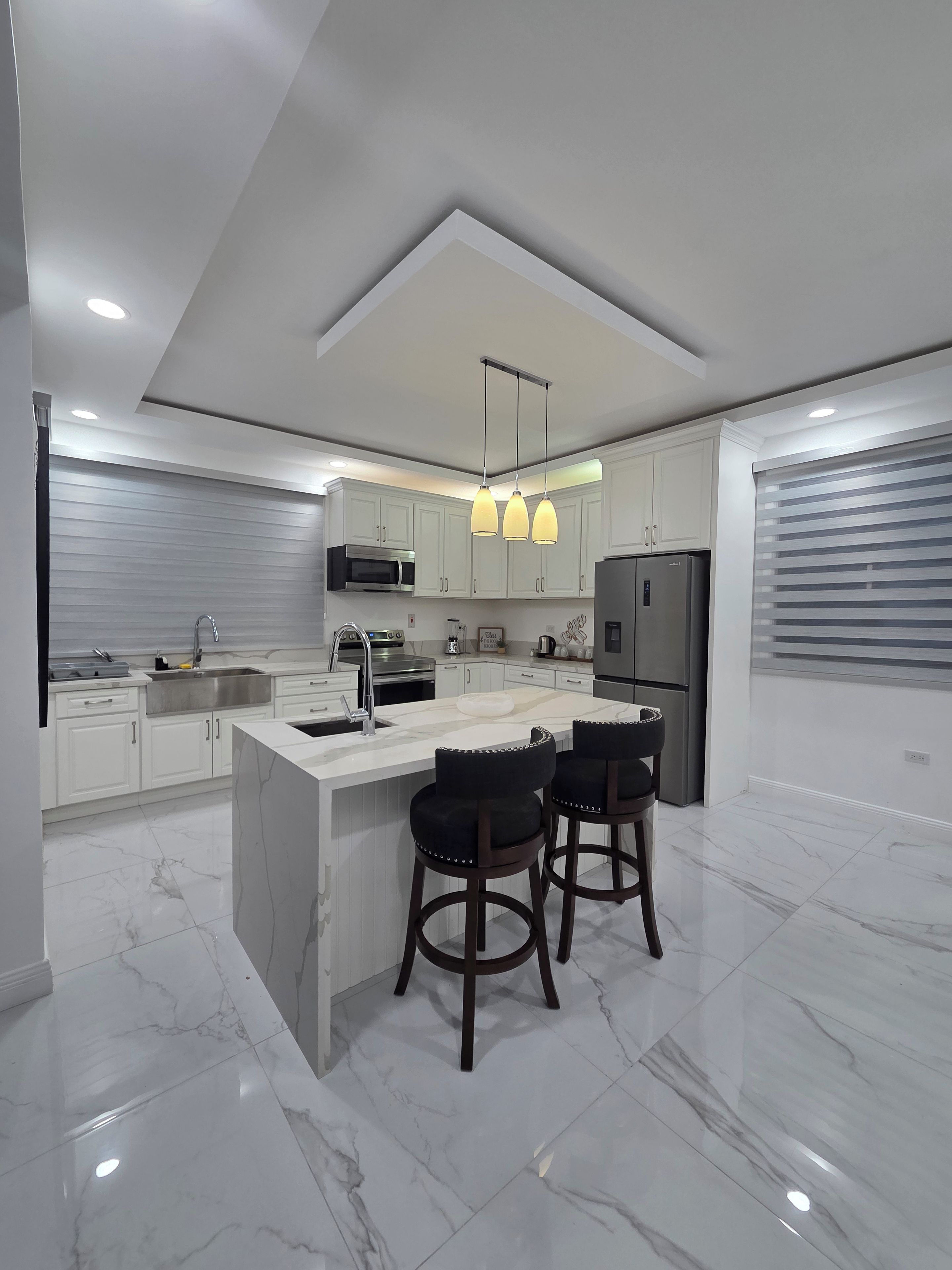 A modern kitchen with a central island, white cabinetry, stainless steel appliances, and pendant lighting.