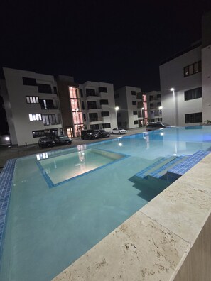 A swimming pool with a tiled deck, surrounded by modern buildings with multiple balconies and windows. - Charisma Airbnb (Kingston)