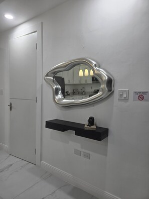 Et badeværelse med en hvid dør, et spejl på væggen, en sort hylde med en lille figur, og et skilt med teksten 'Rygning og dampning forbudt'.