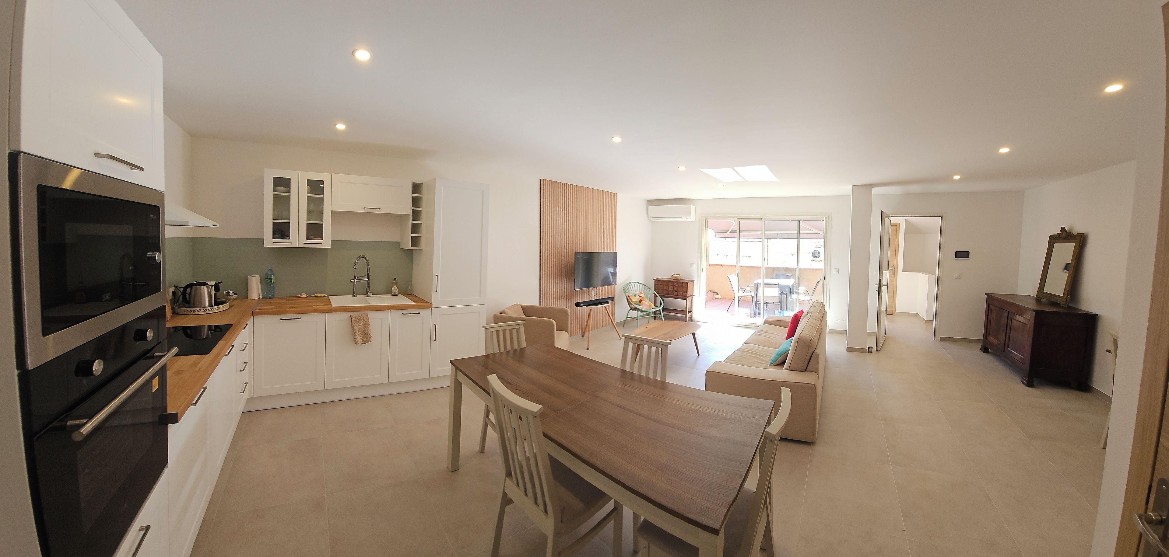 A modern kitchen with a dining area, a TV, and a large window.
