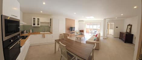 A modern kitchen with a dining area, a TV, and a large window.