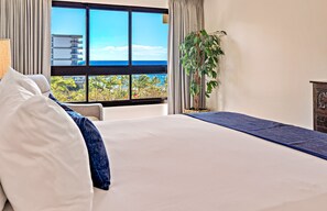 A hotel room with a large window offering a view of the ocean and palm trees. - Maui Resort Rentals: Expansive 5BR Oceanview Retreat for 16 on Kaanapali Beach (Lahaina)