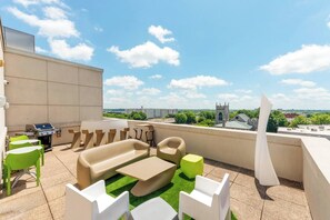 Terrassa al terrat amb seients exteriors, una barbacoa i vistes a una ciutat que inclou una torre d'església.