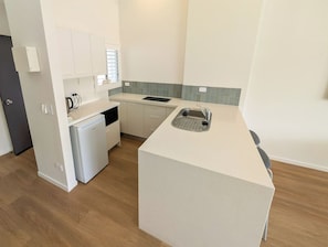 A compact kitchen with a built-in dishwasher, a sink, and a small refrigerator. - Serenity Seas 1 Bed Escape-close to Hastings St (Noosa Heads)