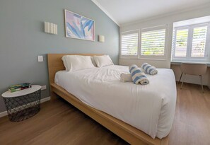 Un dormitorio con una cama grande, una mesita de noche, una silla y una ventana con persianas.