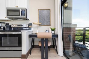 A compact kitchen with a microwave, stove, and dining area with a chair and table. - The Eighth | Luxury Penthouse in Fourth Ward (Charlotte)