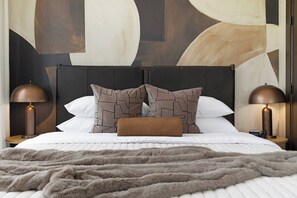 A neatly made bed with a patterned pillow, a fluffy blanket, and two bedside lamps. - The Eighth | Luxury Penthouse in Fourth Ward (Charlotte)