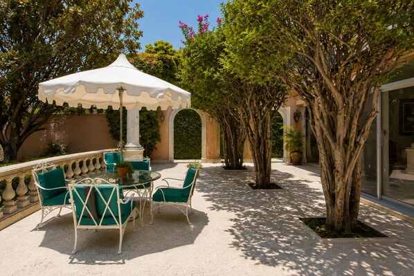 An outdoor patio with a round table and chairs, a white canopy, and trees.