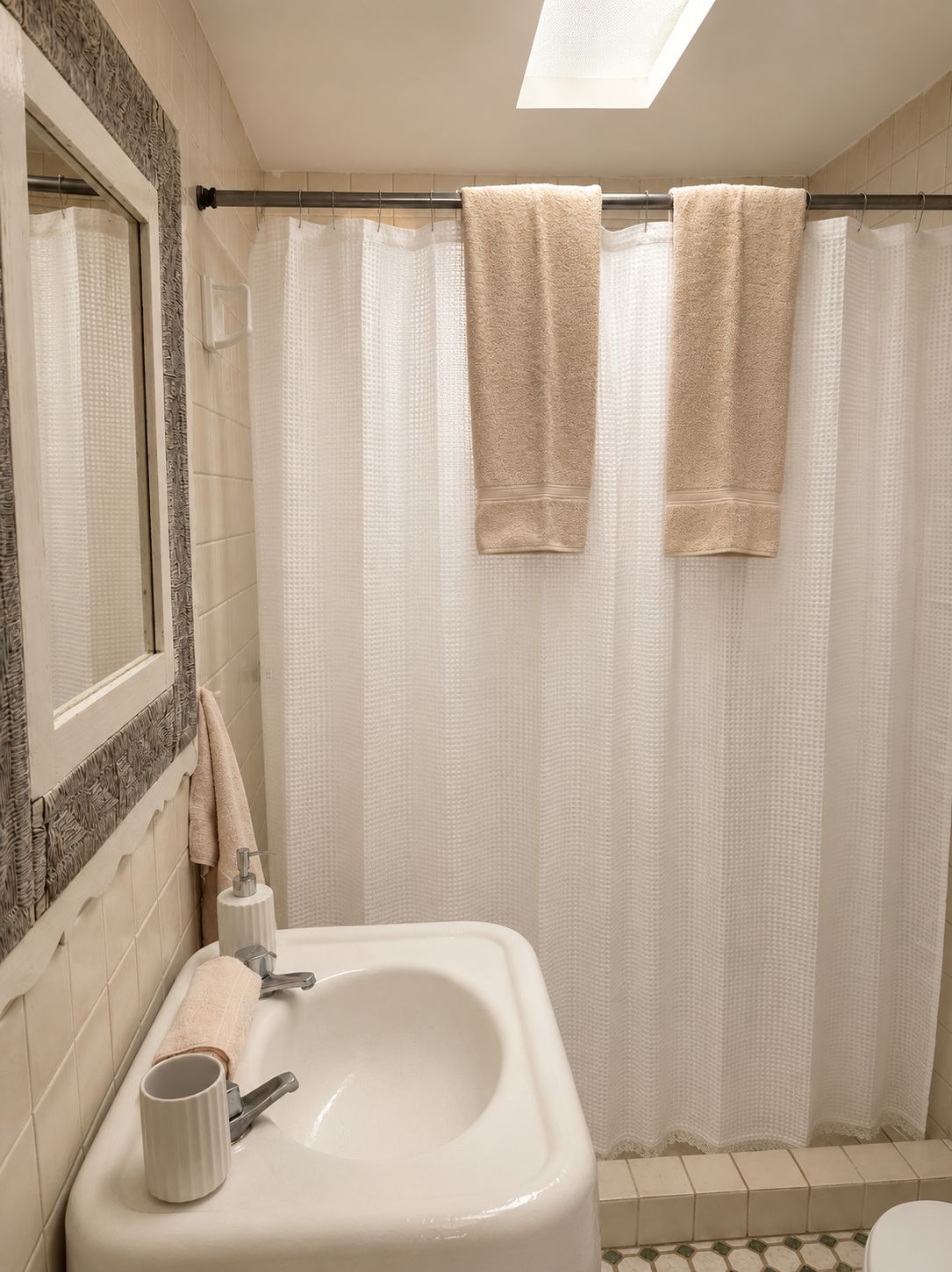 Un baño con lavamanos blanco, un espejo y una cortina de ducha.