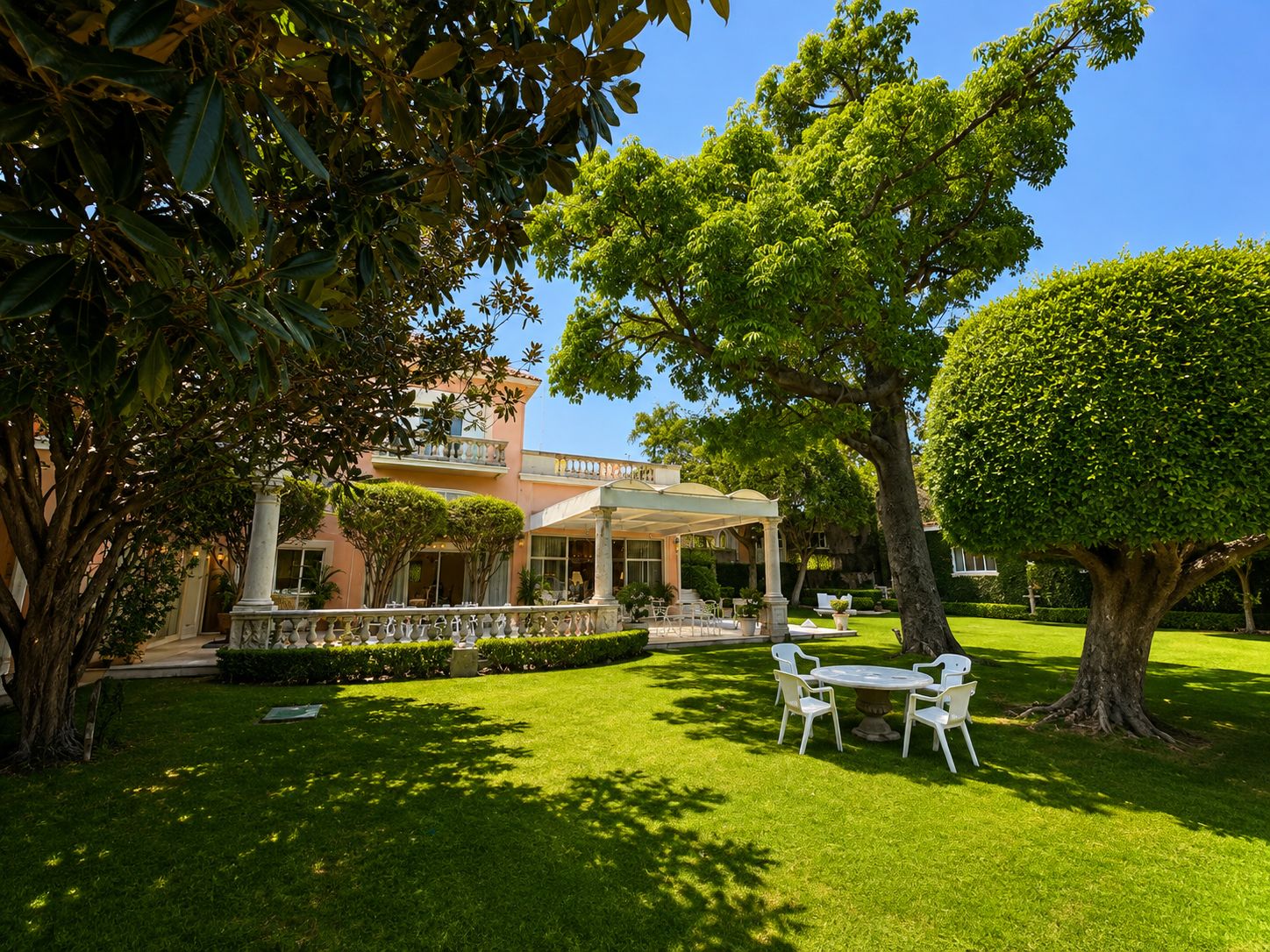 Un jardín bien cuidado con un patio, un árbol grande y un edificio con entrada cubierta.