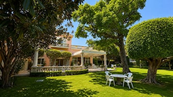 Un jardín bien cuidado con un patio, un árbol grande y un edificio con entrada cubierta.