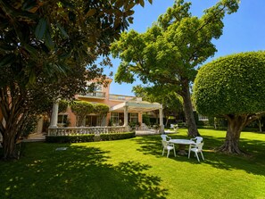 Un jardín bien cuidado con un patio, un árbol grande y un edificio con entrada cubierta.