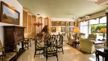 A spacious living room with a grand piano, a dining area with ornate furniture, and a large window offering a view of the outdoors.