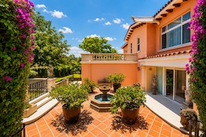 A courtyard with a fountain, potted plants, and a building with large windows. - Casa Carlota with Pool & Garden (Cuernavaca)