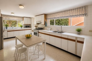 Cocina con gabinetes blancos, pileta doble, microondas y estufa. Hay una ventana con vista a follaje.