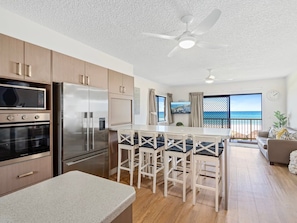 A modern kitchen with a central island, bar stools, and a view of the sea through large windows. - Palm Beach - Beachfront 3 Bedroom! (Palm Beach)