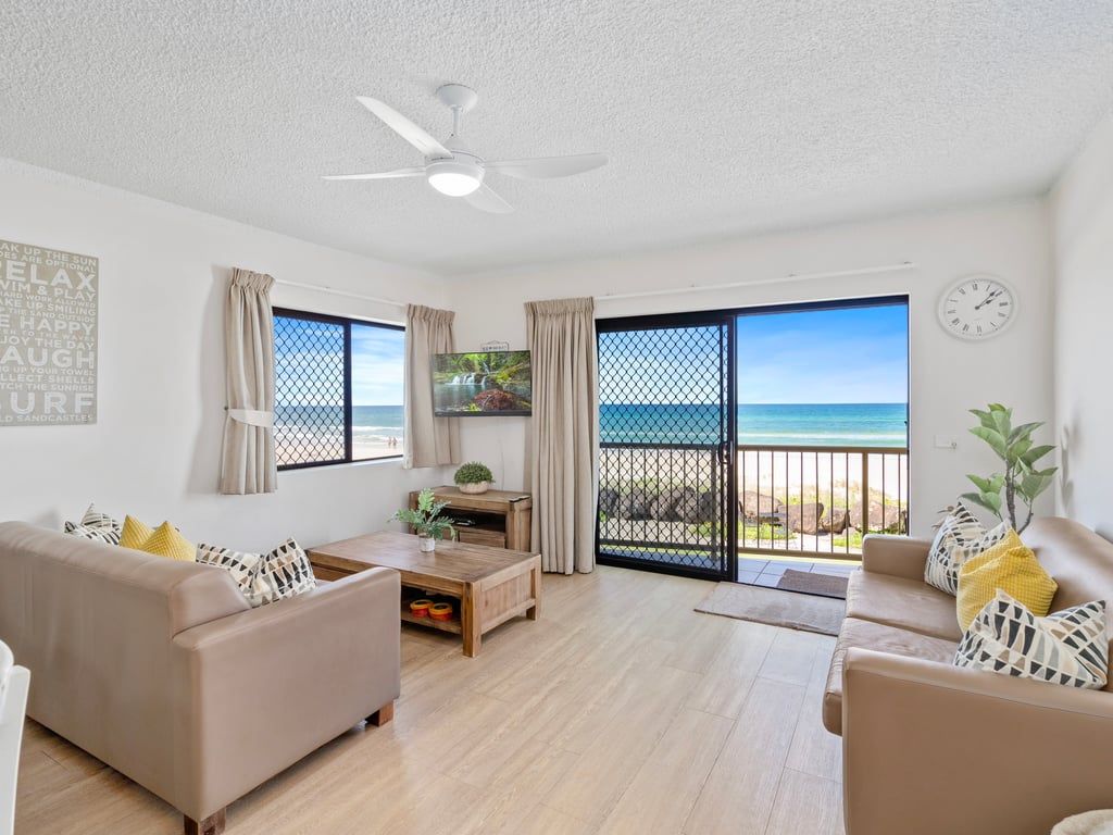 Un salon moderne doté d’une grande fenêtre, d’un ventilateur de plafond et offrant une vue sur la plage.