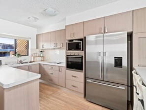 A modern kitchen with stainless steel appliances, light wood cabinets, and a large island. - Palm Beach - Beachfront 3 Bedroom! (Palm Beach)