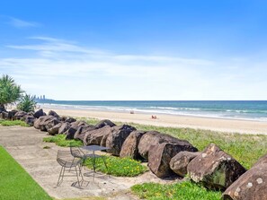 A coastal walkway with large rocks, a table with chairs, and a view of the beach and ocean. - Palm Beach - Beachfront 3 Bedroom! (Palm Beach)