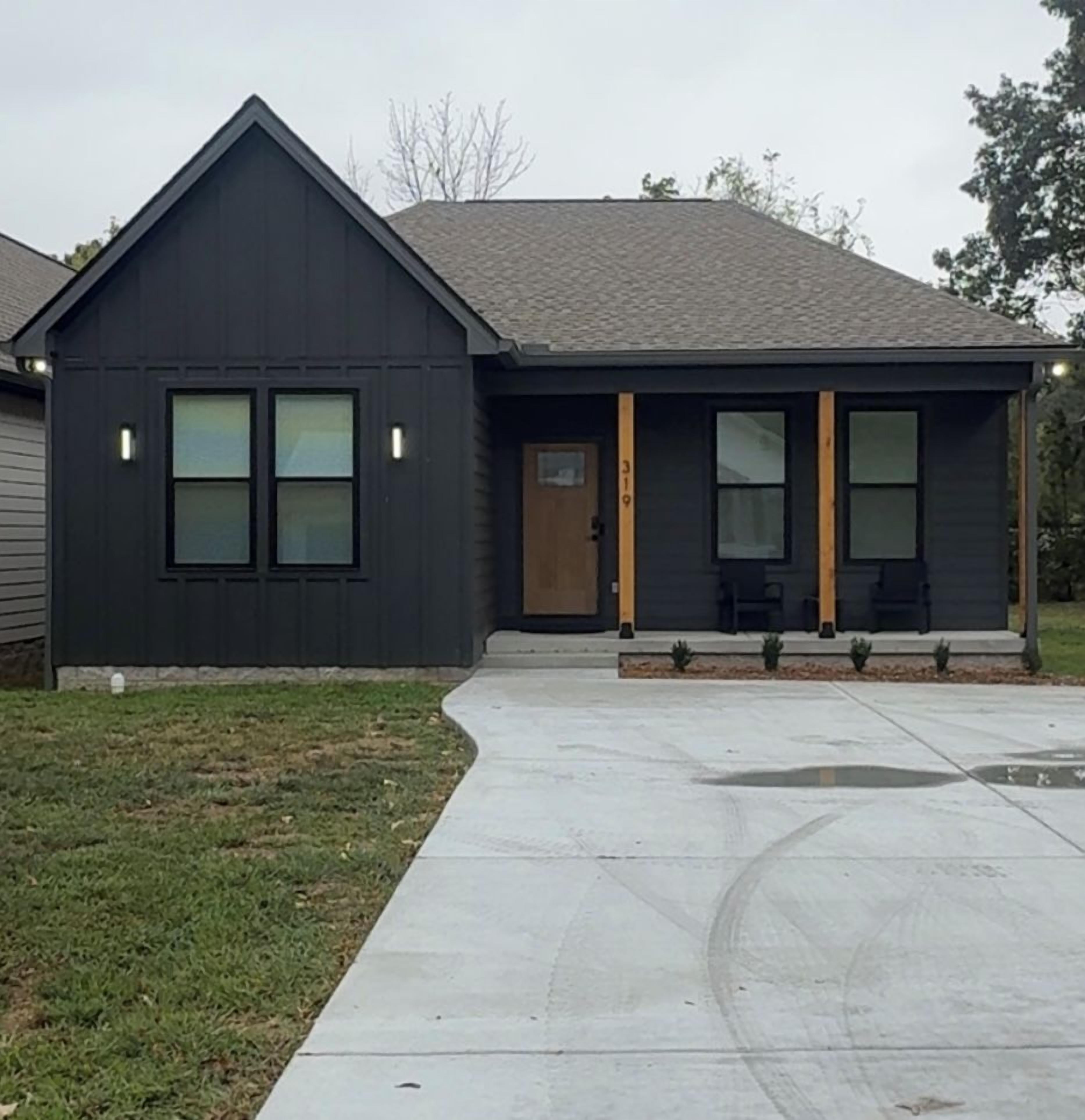 A modern two-story house with a dark facade, a front porch with seating, and a visible address number.