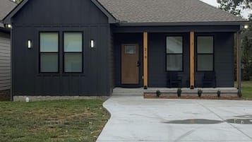 A modern two-story house with a dark facade, a front porch with seating, and a visible address number.