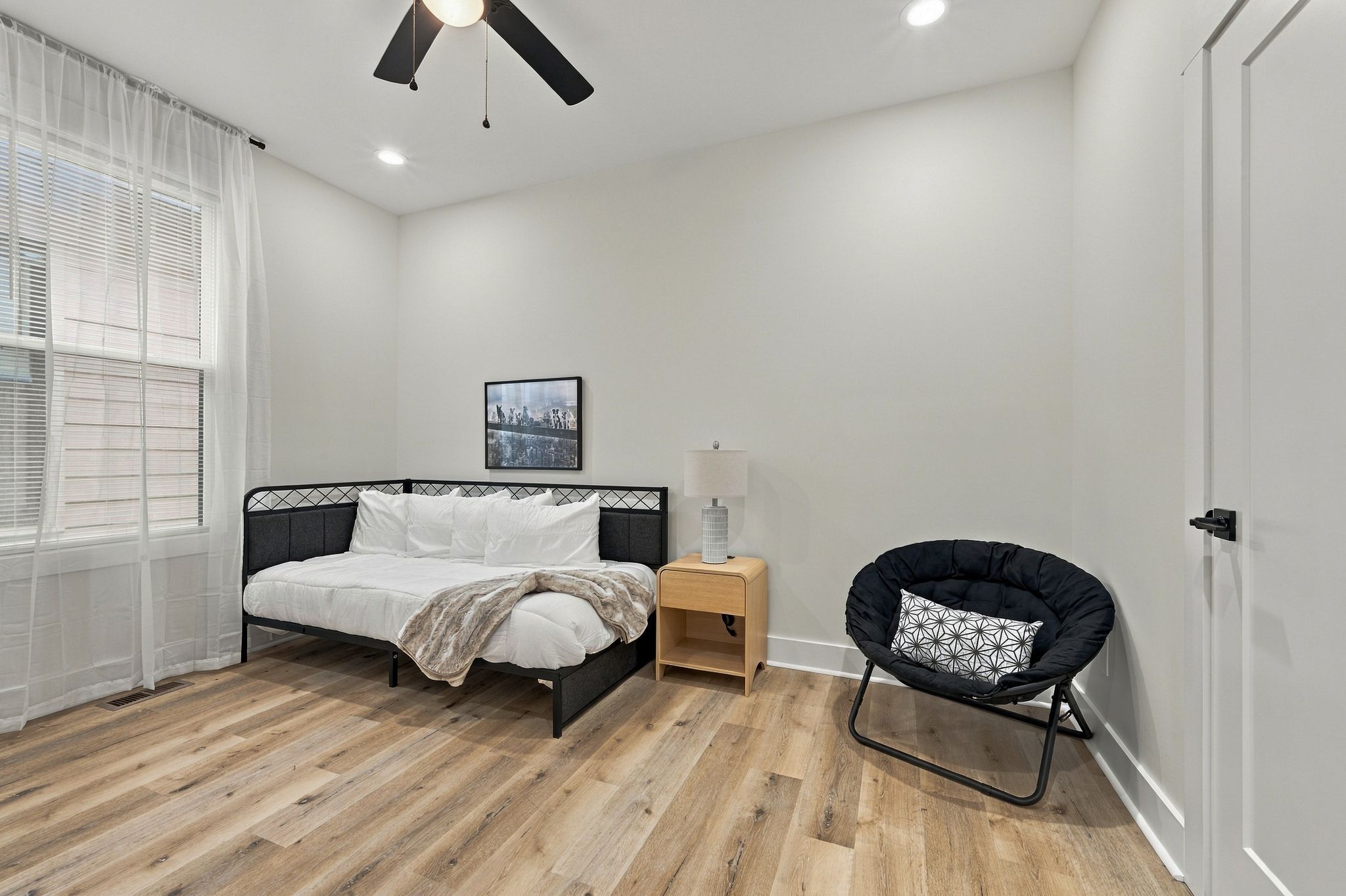 Un dormitorio con cama, mesita de noche, lámpara, sillón y ventilador de techo.